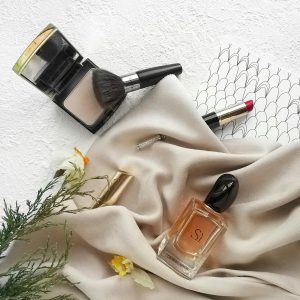 Luxurious flat lay photo featuring makeup products, perfume, and elegant fabric for a sophisticated feel.